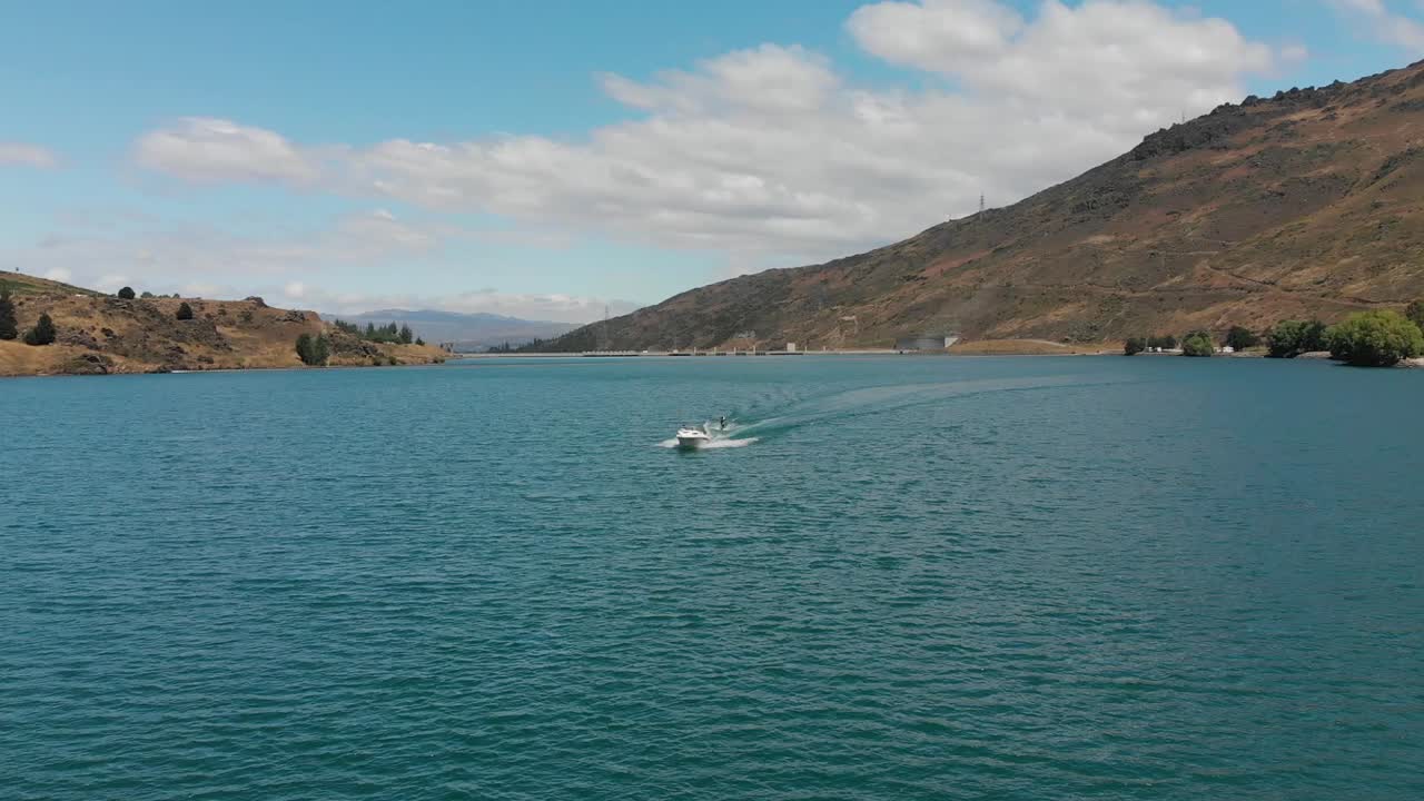 esquí acuático detrás de un barco en el lago dunstan cerca de la represa clyde, otago central, nueva zelanda con montañas y nubes en el fondo