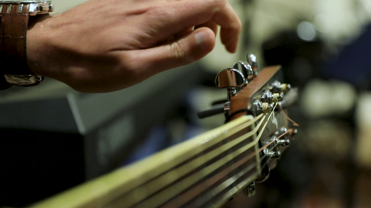 A man with watch tunes a guitar - close up