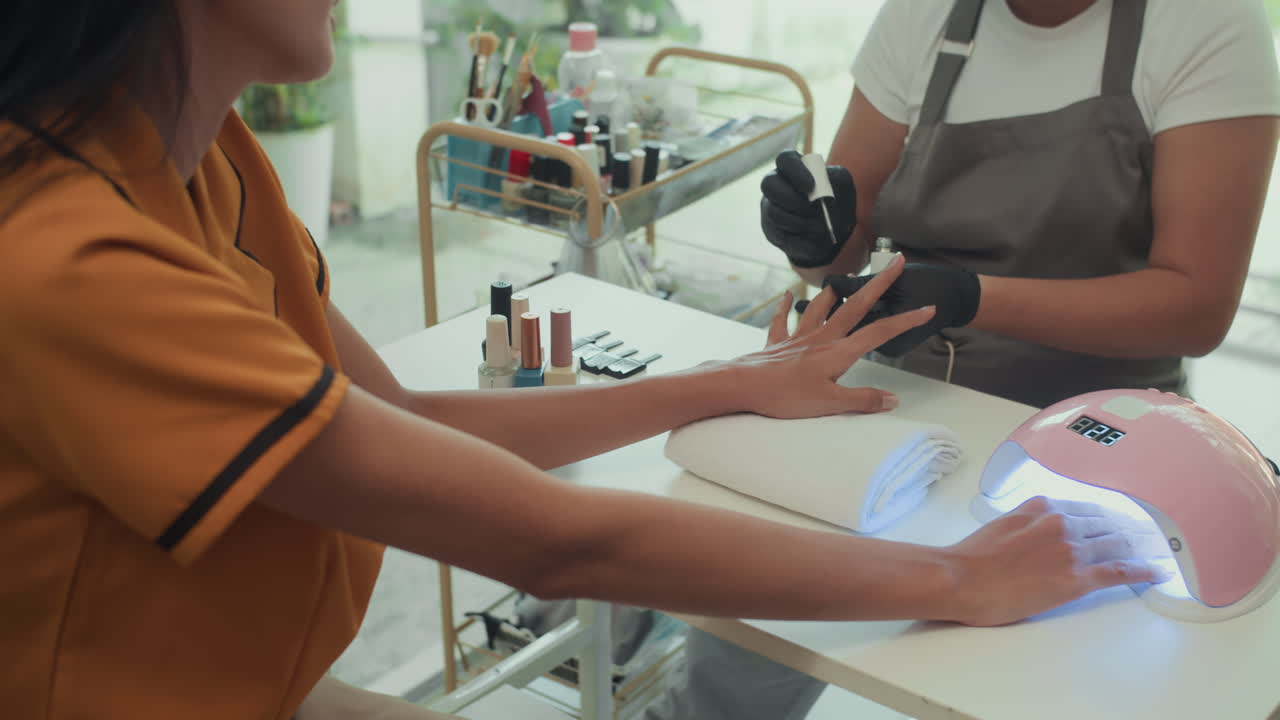 Woman Getting Nails Covered and Holding Hand in UV Lamp during Manicure Session