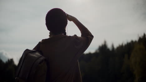 woman with backpack shielding eyes in forest