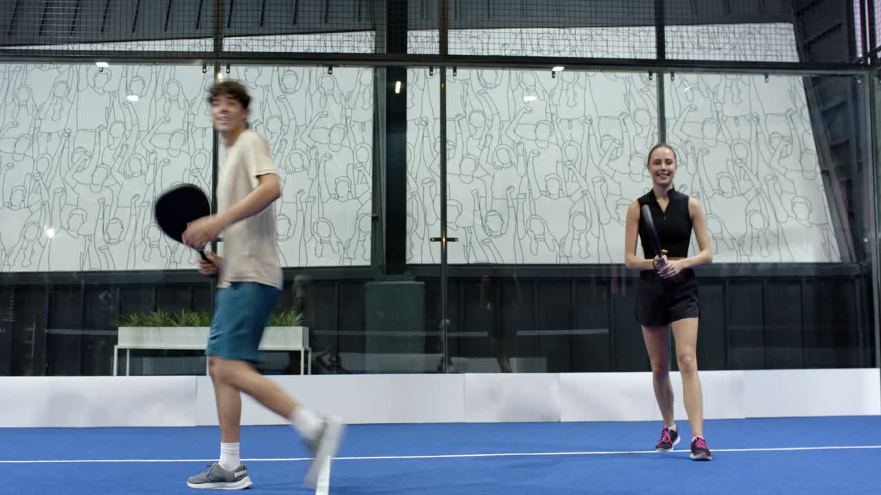 Young diverse athletes playing padel tennis on blue indoor court, enjoying friendly match