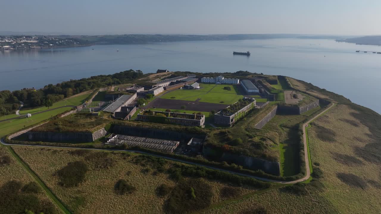 Spike Island, County Cork, Ireland, September 2024. Drone clockwise orbit above the fortifications of the prison with museum at center and barge crossing open waters, Corkbeg and Whitegate on horizon