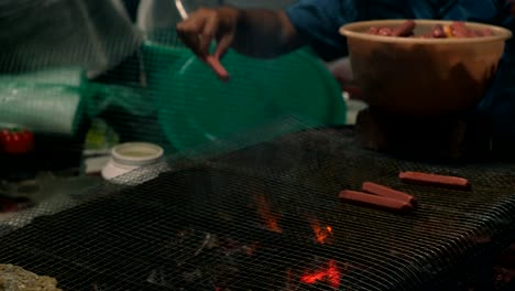 View-of-people-placing-sausages-on-top-of-BBQ-Grill-to-be-cooked-at-night