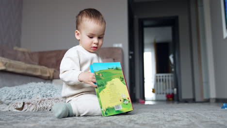 beautiful toddler playing with a colorful book. adorable kid in white suit looks through the bright pictures.