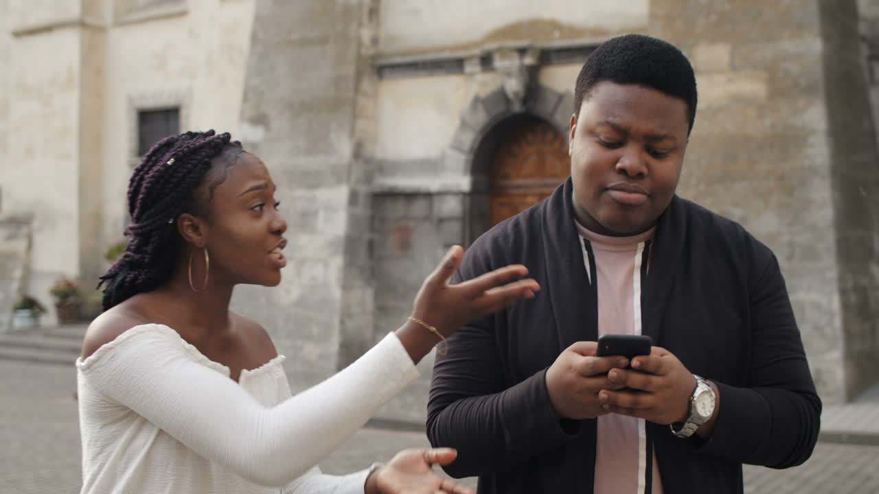 African American couple arguing while one uses a phone