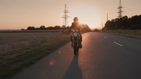 the silhouette of a motorcyclist leaving the city at sunset