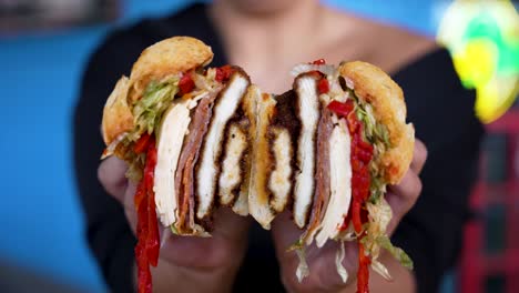 close up in 4k of a chicken cutlet sandwich with roasted peppers dripping out that's just been cut in half and opened to reveal the filling by hands with a perfect manicure