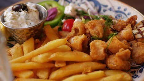 fork picks feta cheese, tzatziki and fries from plate of greek food