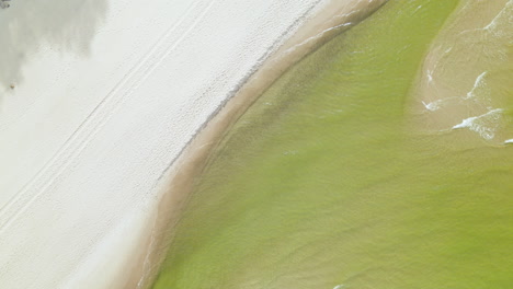 una playa de verano en la costa de polonia, las mareas verdosas del mar báltico rodando sobre arena blanca, vista aérea