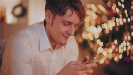 happy man using smartphone at illuminated home during christmas