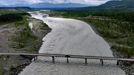 approaching a bridge across the turbulent river crossed by the black car. travel by the wild alaska. aerial view