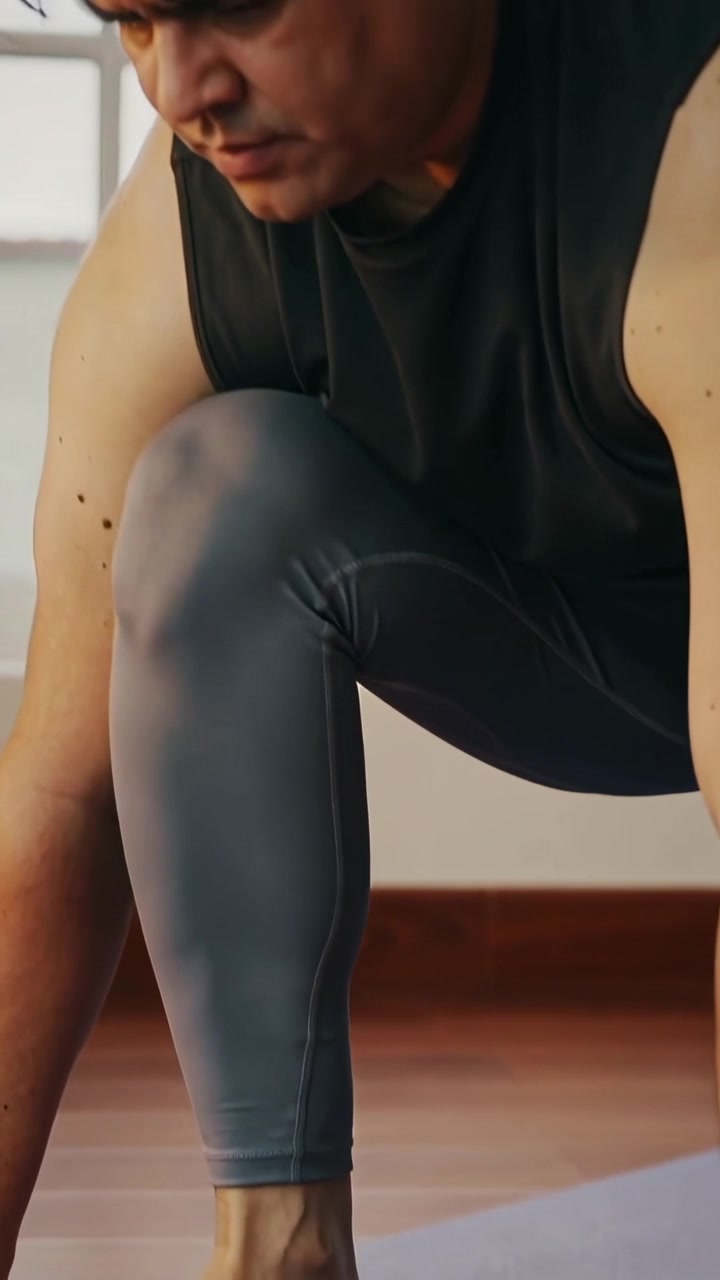 Video verticale: Uomo in maglietta nera e leggings grigi che si tiene in posizione bassa su un tappetino viola a casa per il core