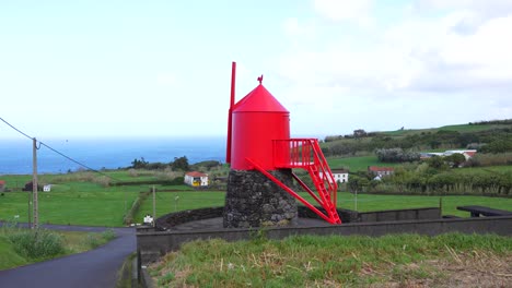 red windmill in green azorean fields by the ocean