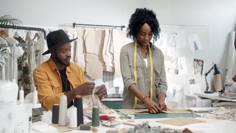 young man designer sitting at desk showing a fabric piece to her colleague female designer