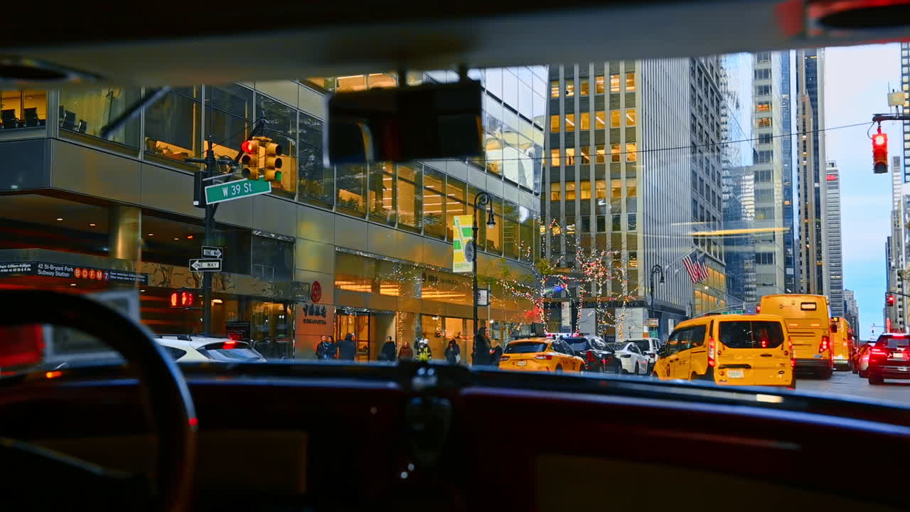Jeg sidder i en bil, der kører ned ad en gade i New York. Udsigten fra forruden viser taxaer, biler, bygninger og folk, der går forbi.