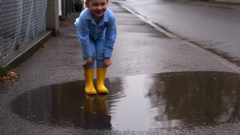 child jumping and splashing in a puddle with yellow rain boots