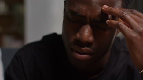 close up of unhappy and depressed young man sitting on sofa at home looking anxious and worried rubbing forehead 4