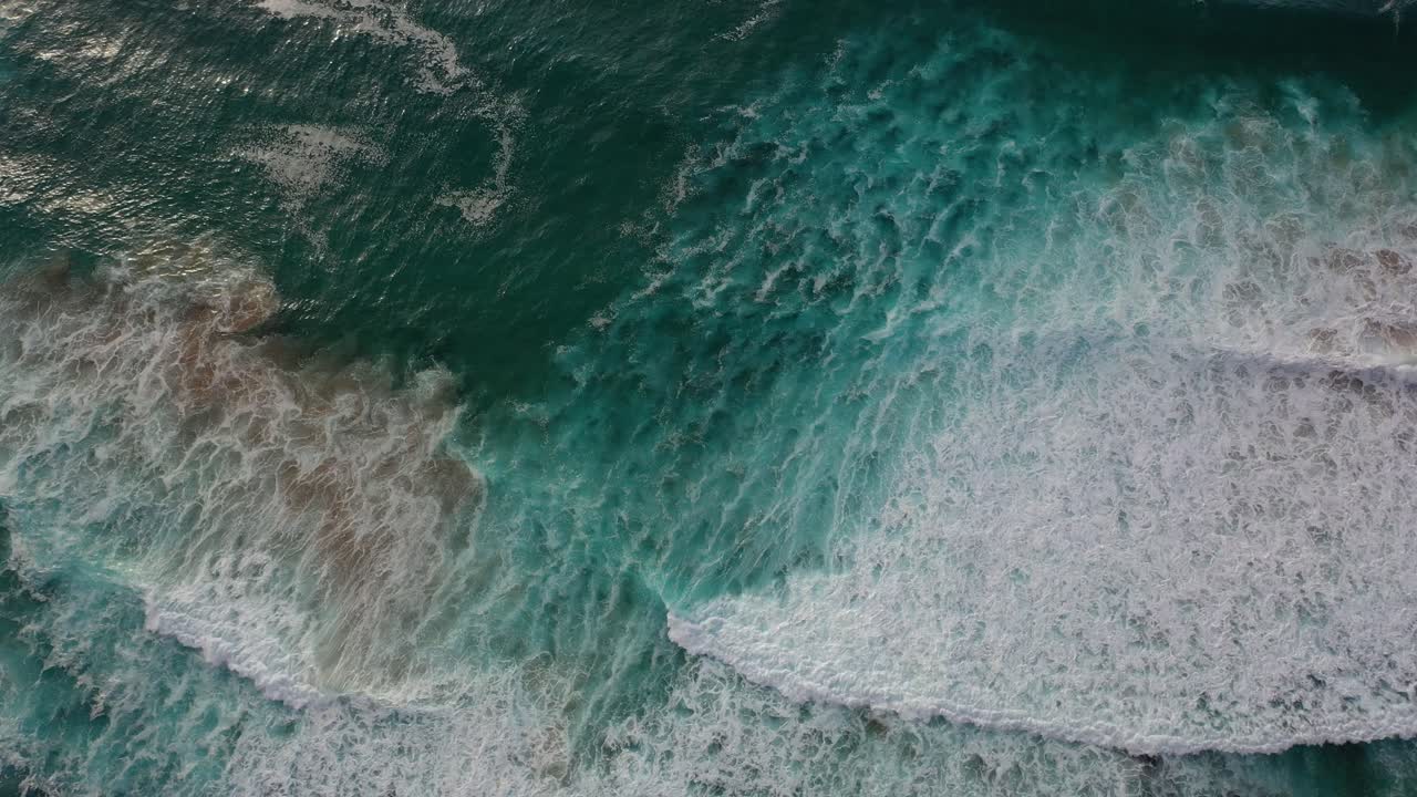 Shot with drone over sea waves in turquoise and white colors and then rising towards the dark blue horizon and the cloudy sky letting the sun's rays pass into the water in the Cantabrian Sea Spain