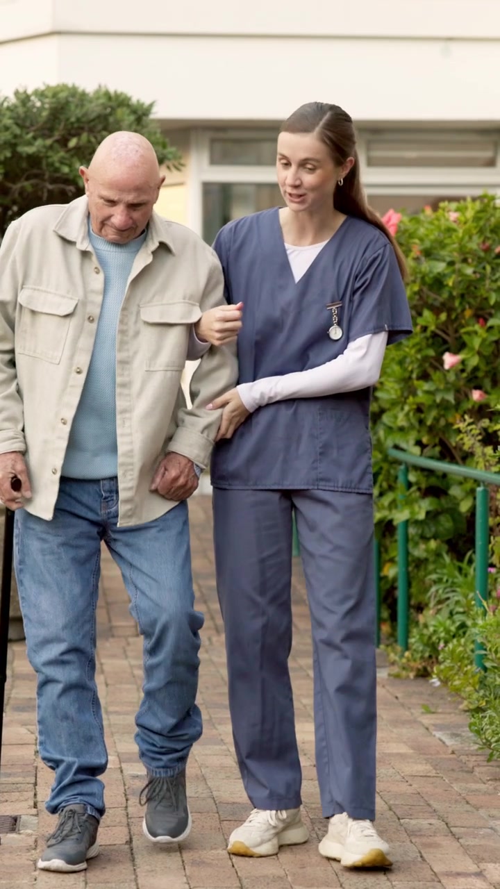 Young Nurse Assisting Elderly Man Walking Outdoors