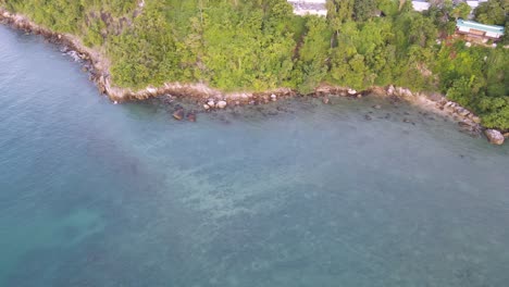 Drone-aerial-slow-pan-up-over-tropical-blue-water-in-Thailand-with-houses-on-the-green-mountainside