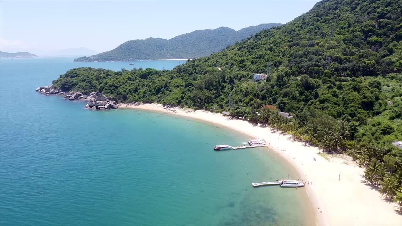 Aerial footage of a pristine beach on an island, showcasing powdery white sand and turquoise waters. Highlights the serene beauty and lush surroundings of this idyllic tropical paradise.
