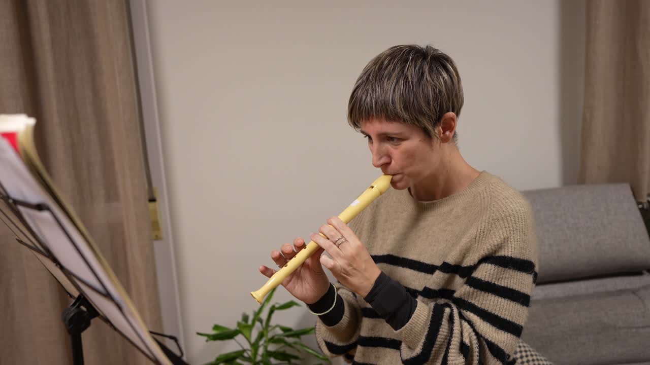 Mulher tocando flauta doce e lendo partitura em casa