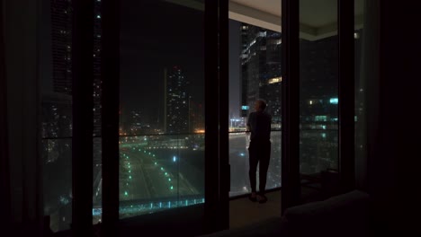 silhouette of a lonely man on a balcony of an apartment overlooking a city - comes inside