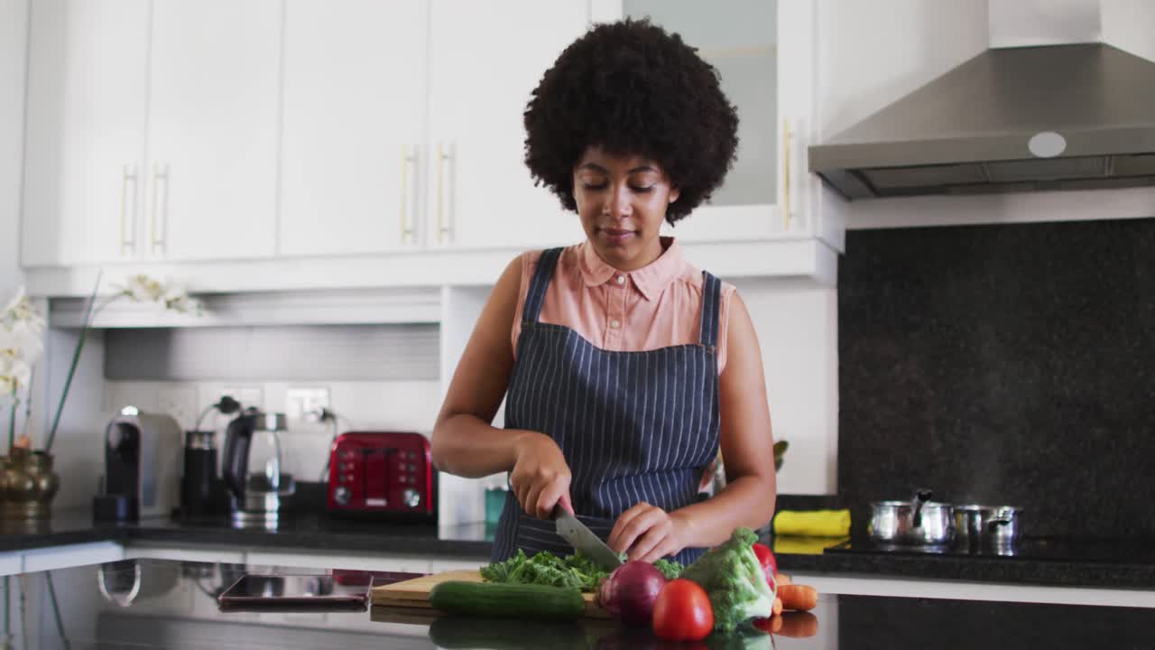 Mulher afro-americana picando vegetais na cozinha de casa.