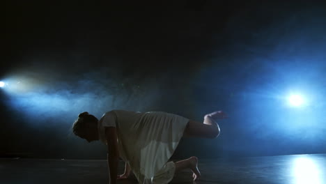 la cámara de zoom se mueve alrededor del escenario con software y humo. chica bailarina bailando en un vestido blanco girando plástico mientras realiza piruetas y rotaciones experimentando emociones y atmósfera dramática.