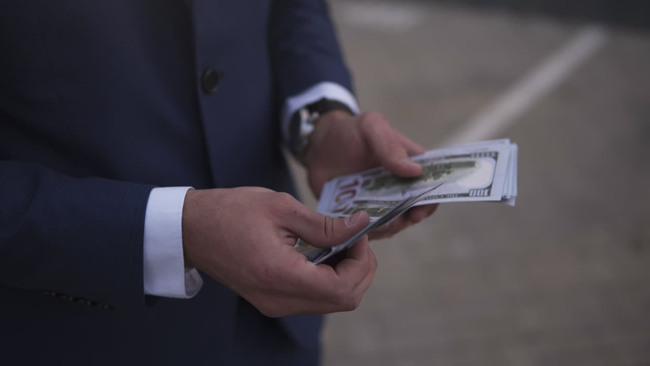 Unrecognizable businessman on the street holding bundle of american money in his hands, counting it. Wealthy male counts hundred