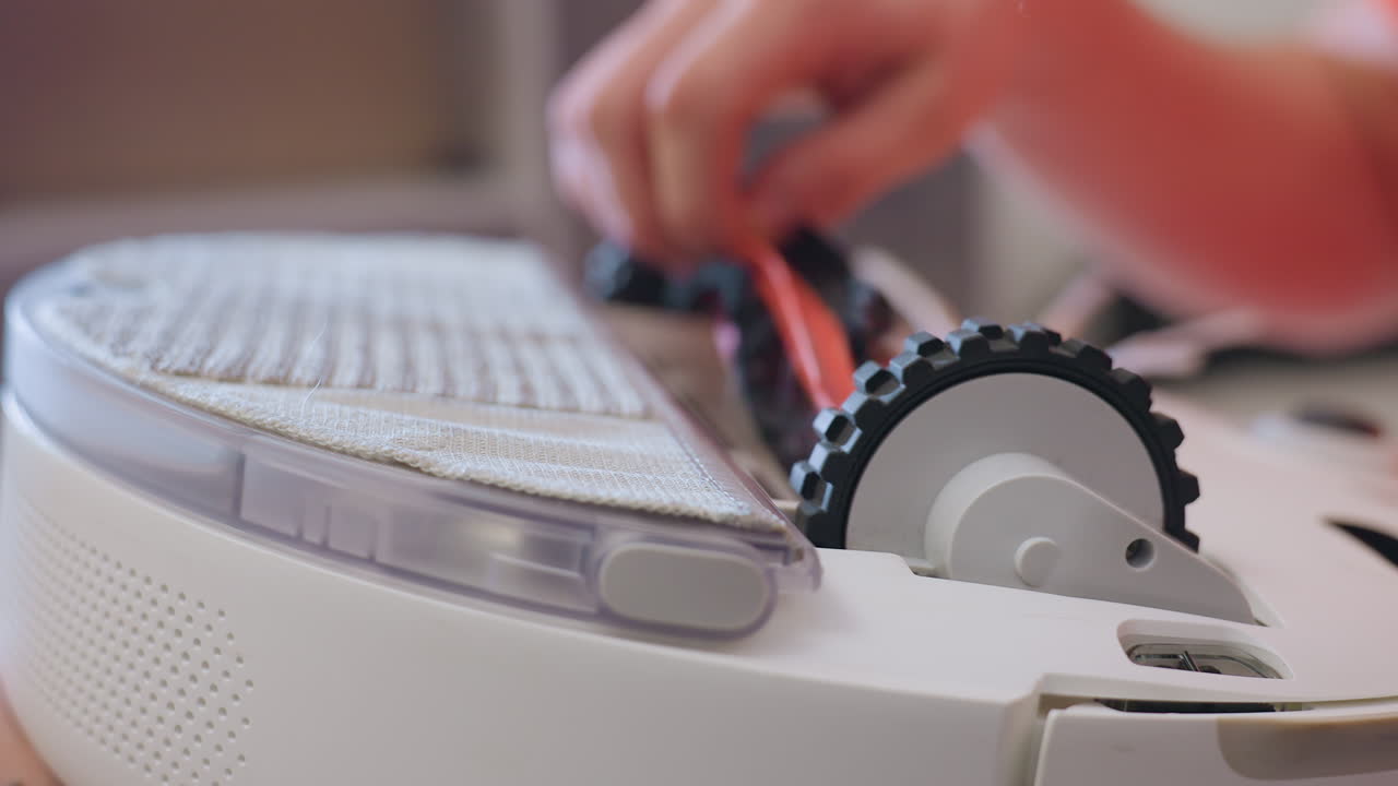 Close up of hands repairing vacuum cleaner wheel, carefully adjusting parts of household device, demonstrating maintenance process, technical repair skill, and attention to functional details