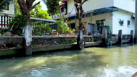 un tranquilo paseo en barco a lo largo del canal khlong lat mayom de bangkok, mostrando casas vibrantes a la orilla del río y vegetación exuberante bajo la brillante luz del día