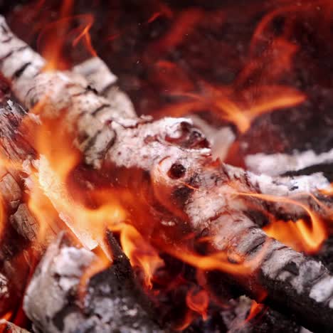 wooden logs in bright flame. smoldered logs with sparks in campfire. wooden stick turning over wooden embers in orange flame. close-up.