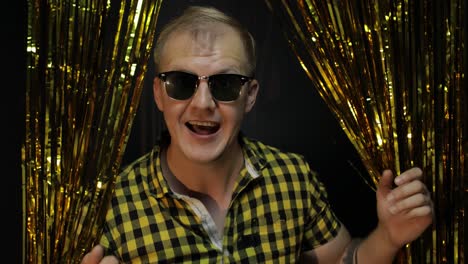 portrait of caucasian man posing on black background. gold shining foil strips. party, music, disco