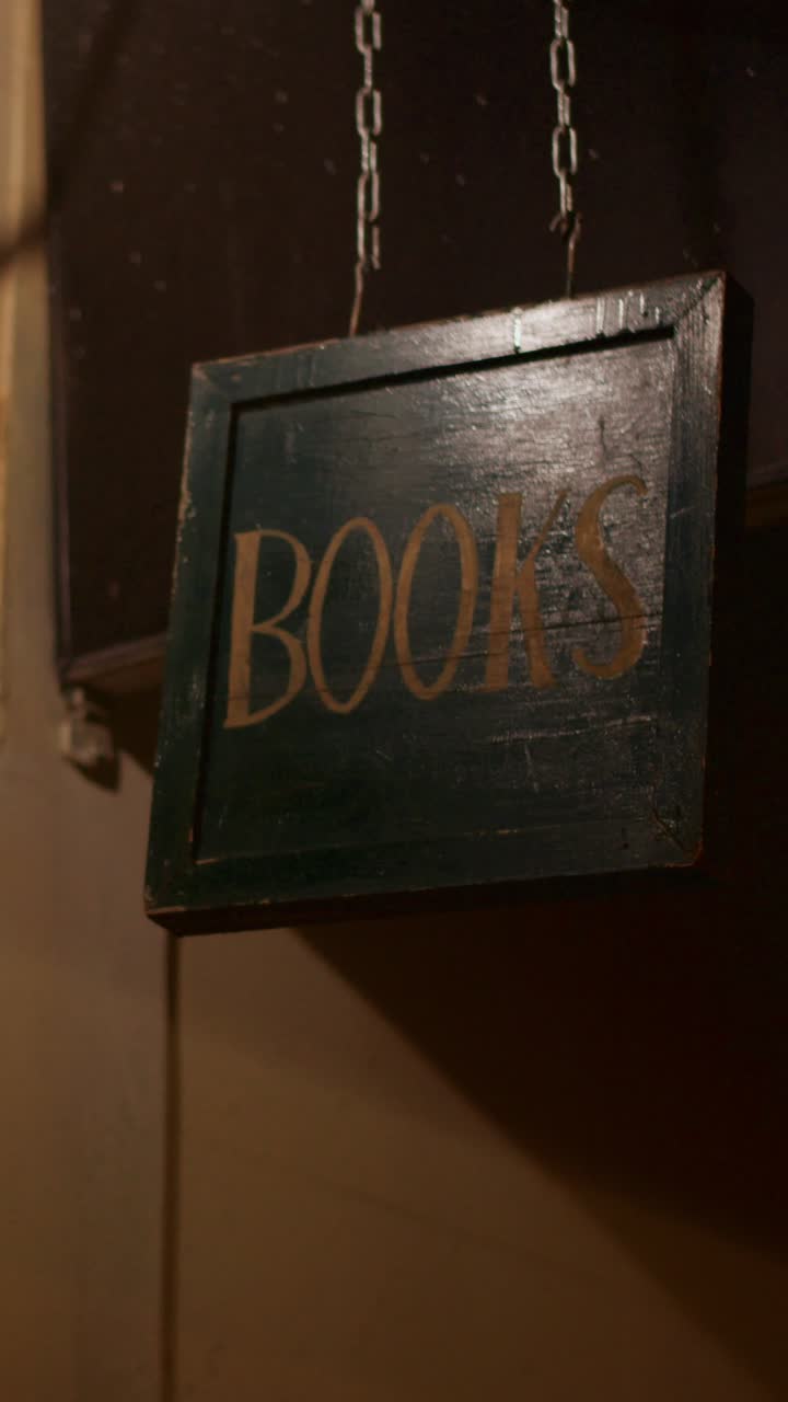 Insegna vintage in legno a forma di libri appesa a catene.