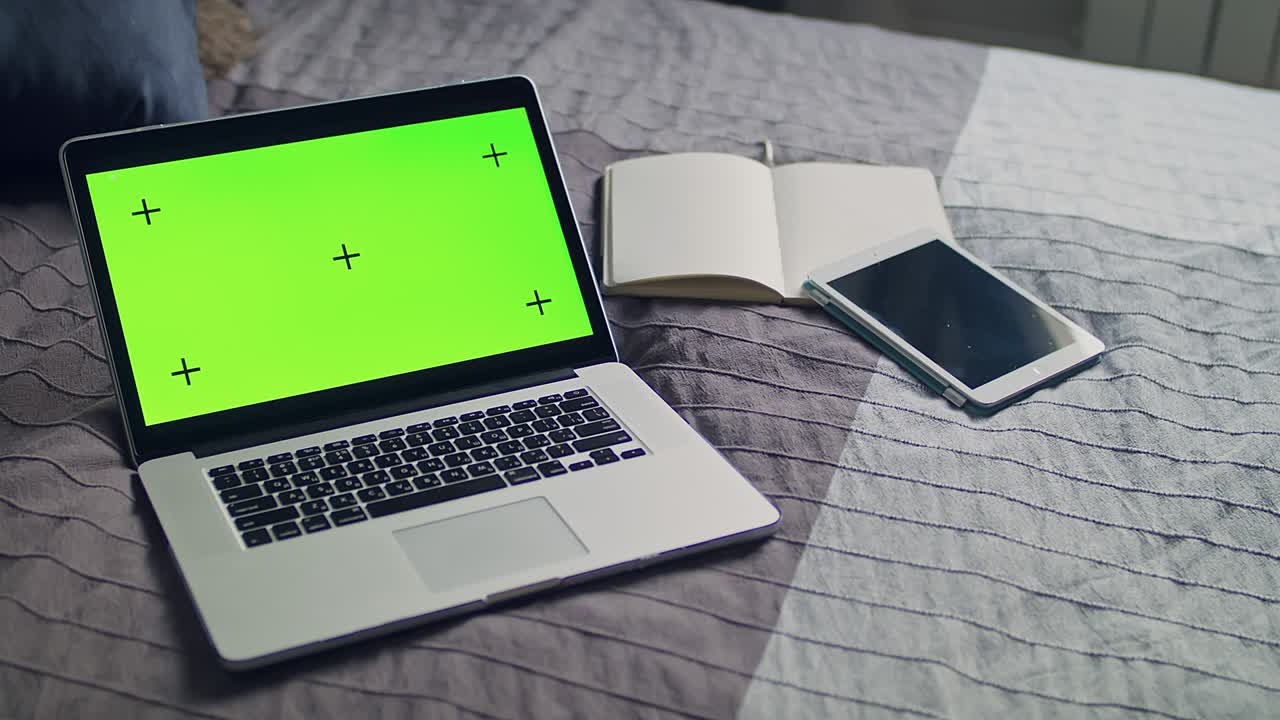 The laptop, notebook with green screen and tracking markers. Mobile tablet lying on the bedspread.