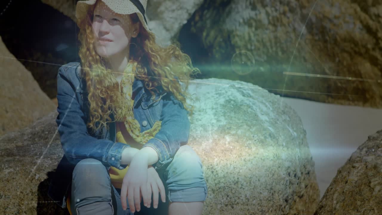 Woman wearing sunhat sitting on beach rock, activating animated data overlays for tech exploration