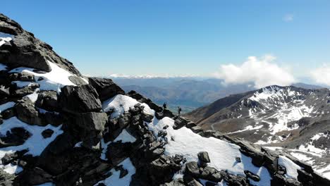 Dos-Excursionistas-Suben-Por-La-Cresta-Nevada-De-La-Cordillera-De-Notables-En-Queenstown,-Nueva-Zelanda.