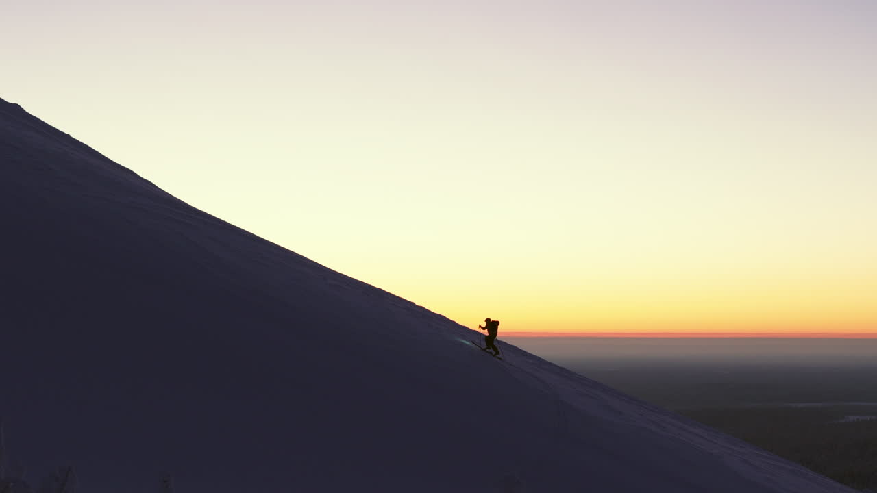 uno sciatore libero si arrampica lungo il bordo della montagna verso la cima mentre l'alba arancione sullo sfondo