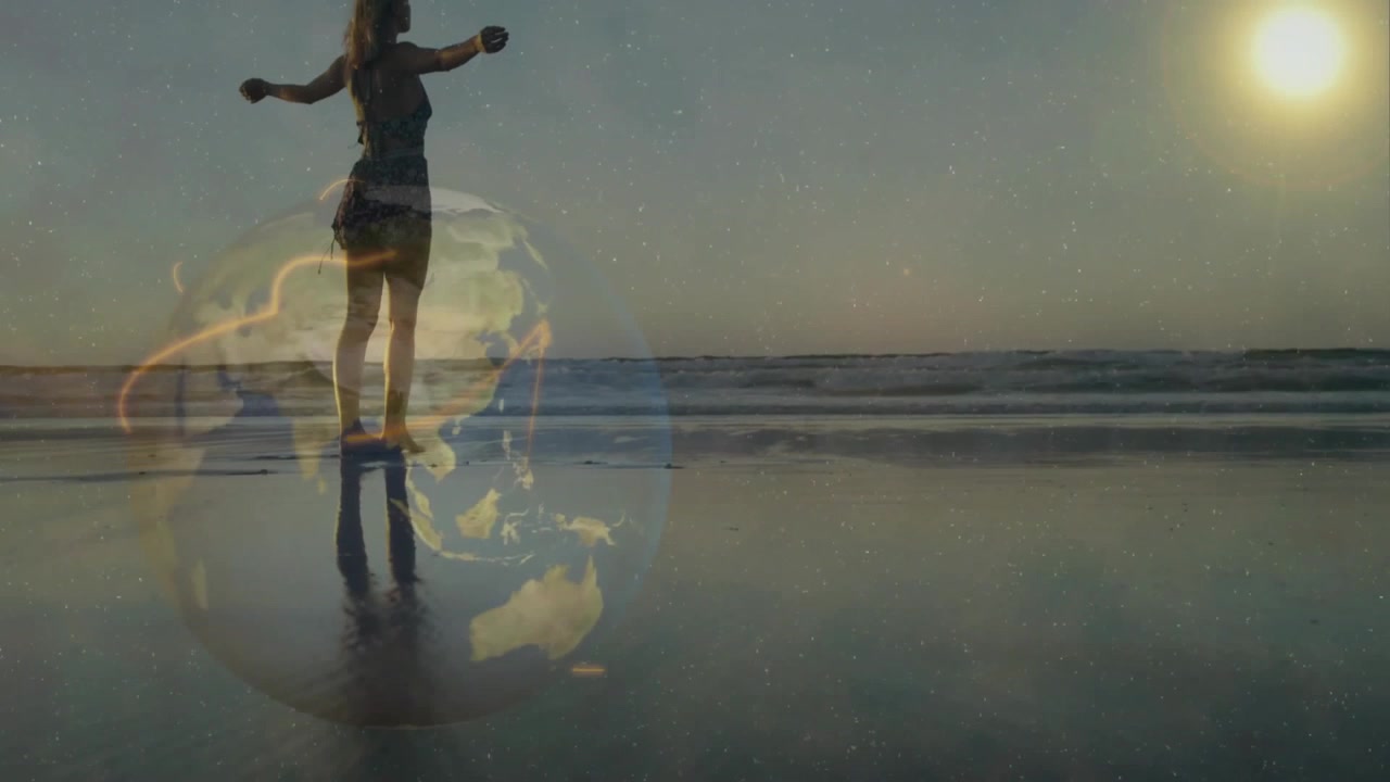 Captura em ângulo baixo de mulher caminhando na areia molhada, com um globo girando sob os pés e dançando sob o pôr do sol