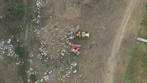 aerial top-down view of two backhoes working and moving rocks at a construction site