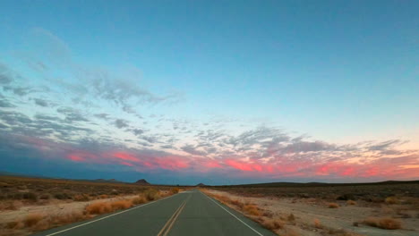 el cielo de la tarde es rosado por la puesta del sol mientras conduce por esta carretera del desierto de mojave - punto de vista