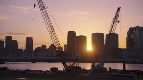 Baukräne-Mit-Der-Stadt-Osaka-Im-Hintergrund-Bei-Sonnenaufgang,-Japan