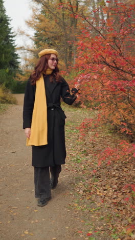 una joven con una boina amarilla y un silenciador explora un camino del bosque, tocando hojas de otoño rojas vibrantes, completamente inmersa en el ambiente sereno