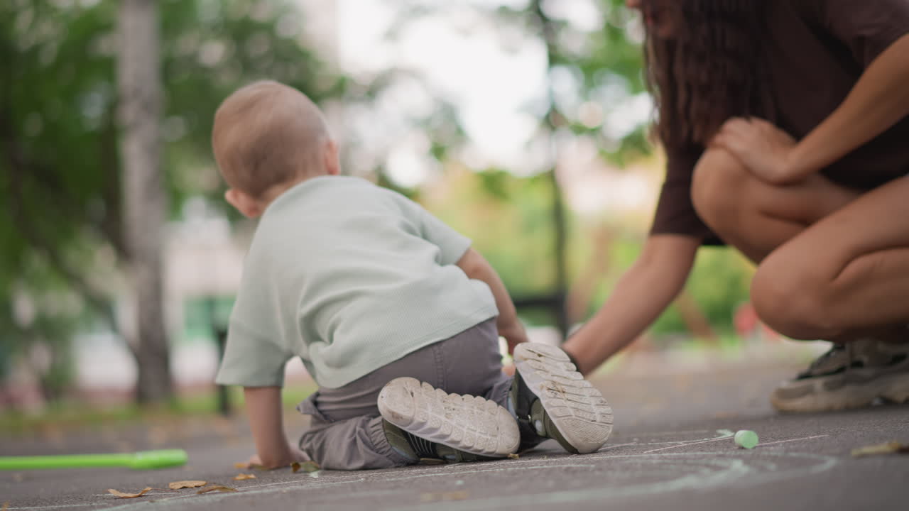 Sviluppo della mobilità infantile in un parco. Un bambino piccolo si esercita a gattonare all'aperto con il supporto premuroso di un adulto, progredendo nelle sue abilità grazie a una figura attenta nell'ambiente del parco.