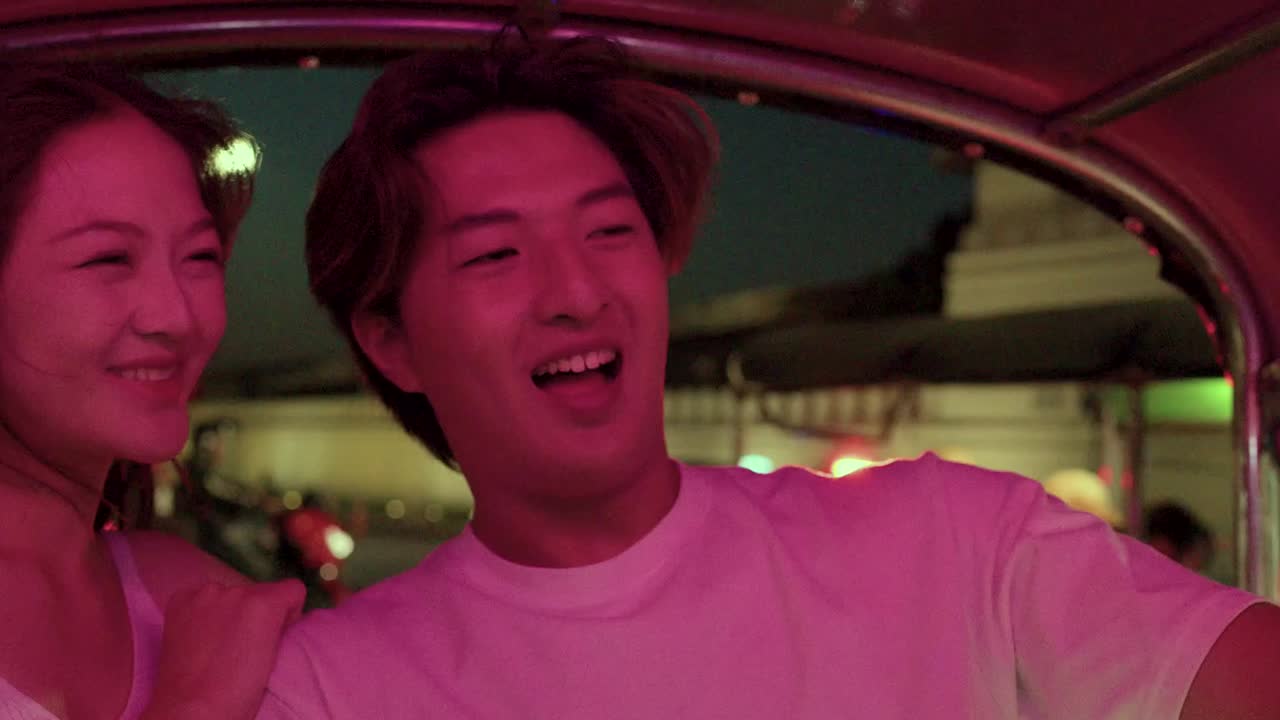 Una giovane coppia sorridente registra un video con lo smartphone durante un vivace giro notturno in risciò per la città