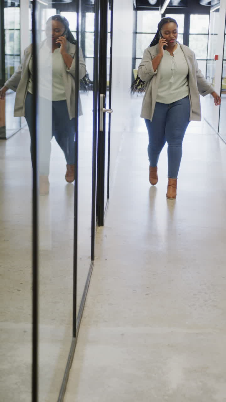 Vertical video of happy african american businesswoman talking on smartphone in office, slow motion
