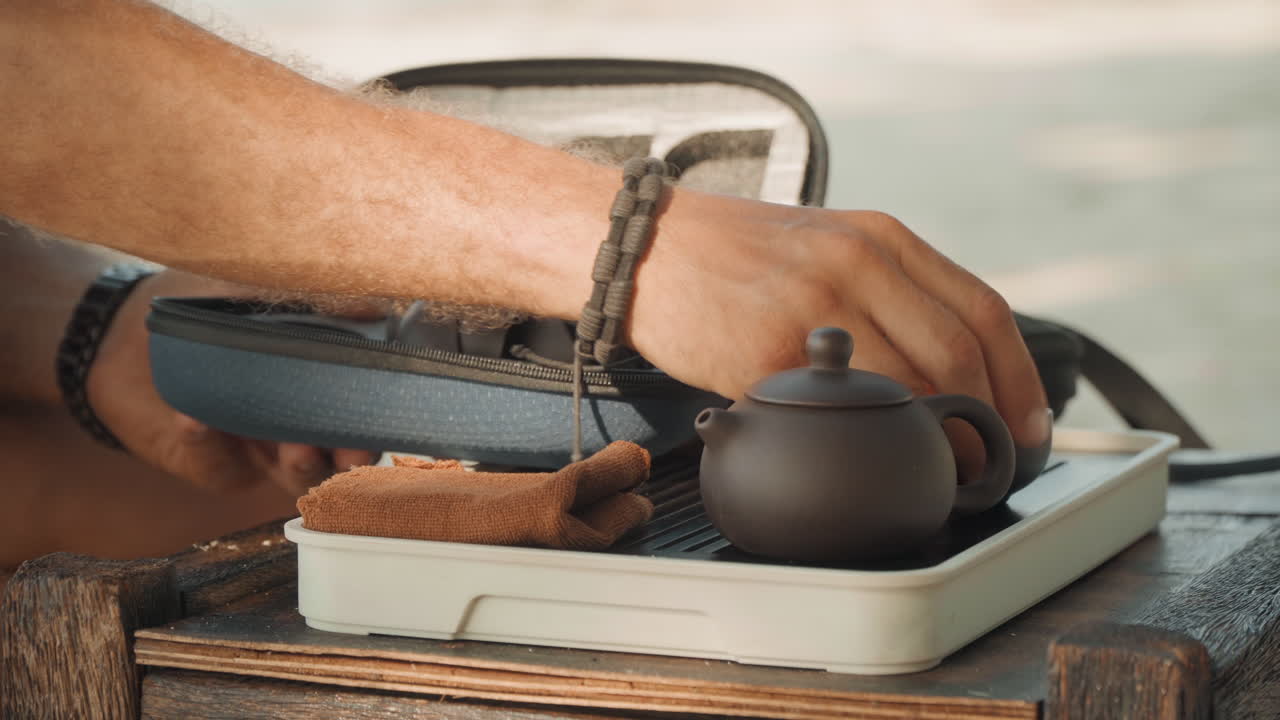 Ambiente oceanico calmo per la preparazione del tè. Scena costiera rilassante con delicate stoviglie da tè e onde leggere. Sfondo oceanico tranquillo mentre le mani organizzano con grazia una tazza da tè tradizionale su un vassoio sabbioso