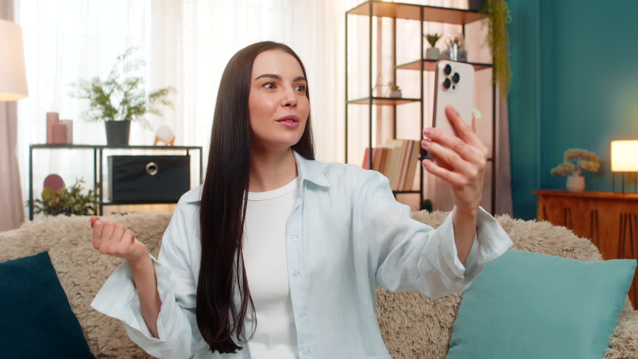 Young woman on sofa having video call laughing and using expressive hand gestures with real emotion