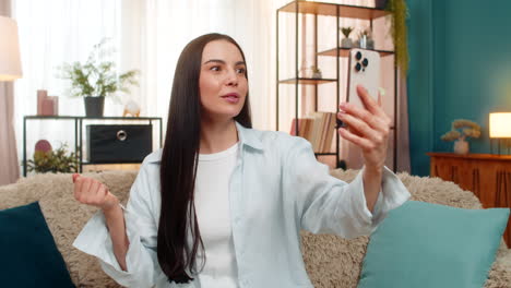 young woman on sofa having video call laughing and using expressive hand gestures with real emotion